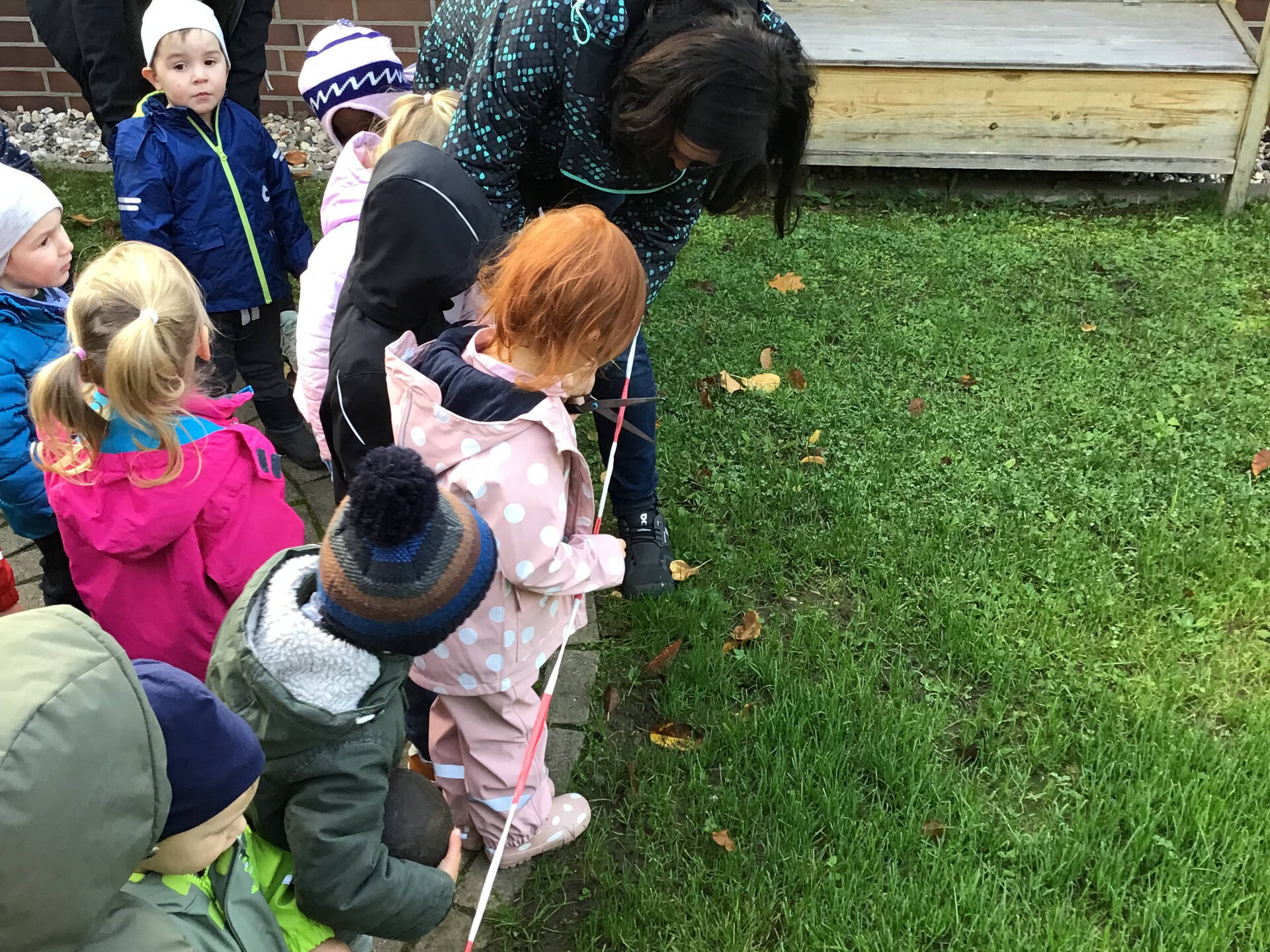 Kinder stehen hinter einem Absperrband und eine Frau hilft es mit einer Schere durchzuschneiden.