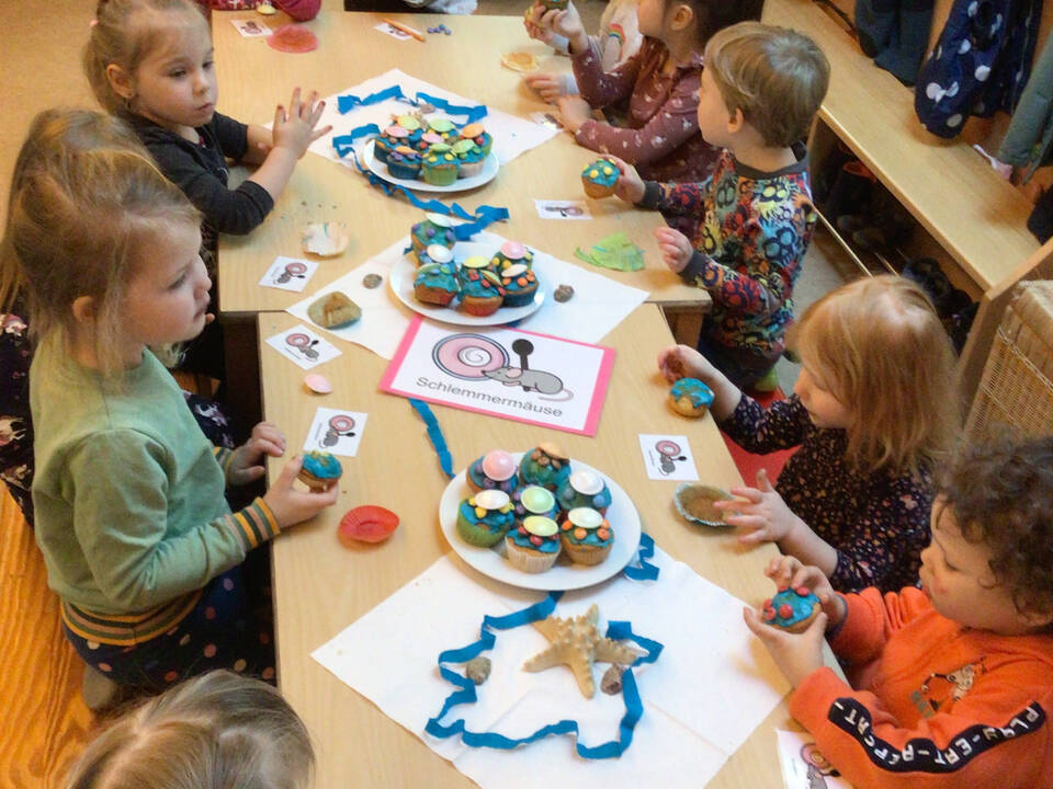Kinder sitzen am gedeckten Tisch und essen Muffins.