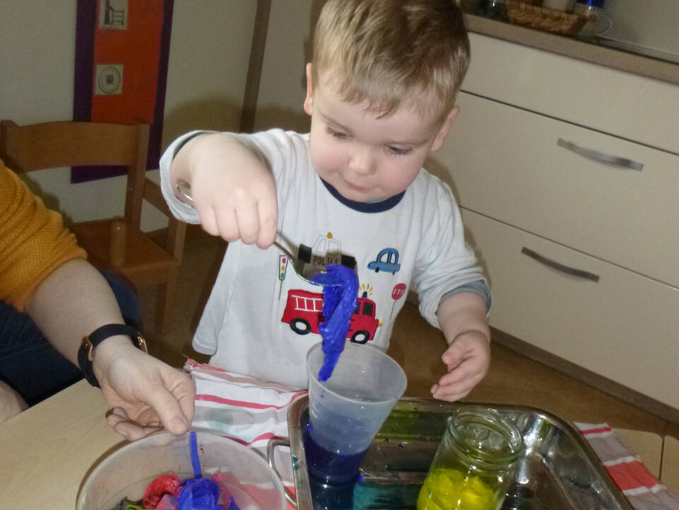 Ein Junge hält einen Löffel mit einem blauen Tuch drauf in der Hand.