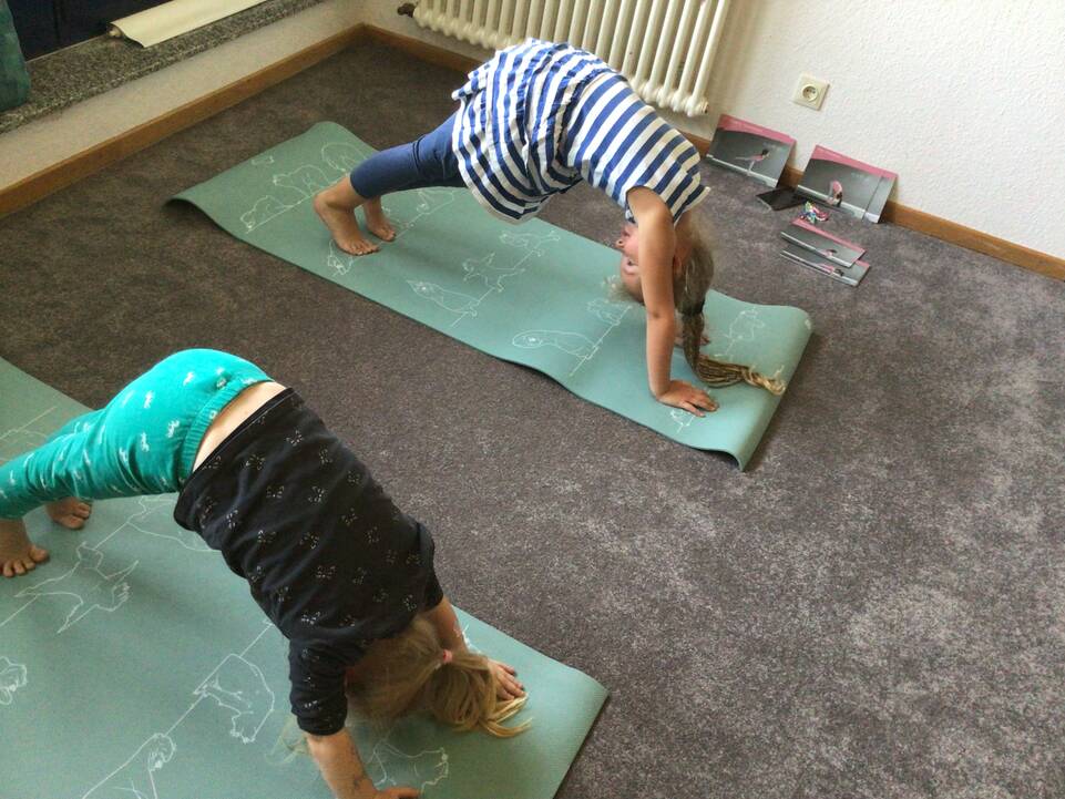 Zwei Kinder auf Matten machen eine Brücke.