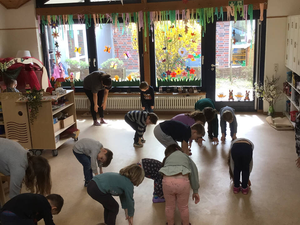 Mehrere Kinder in einem Raum fassen sich im Stehen an die Zehen.