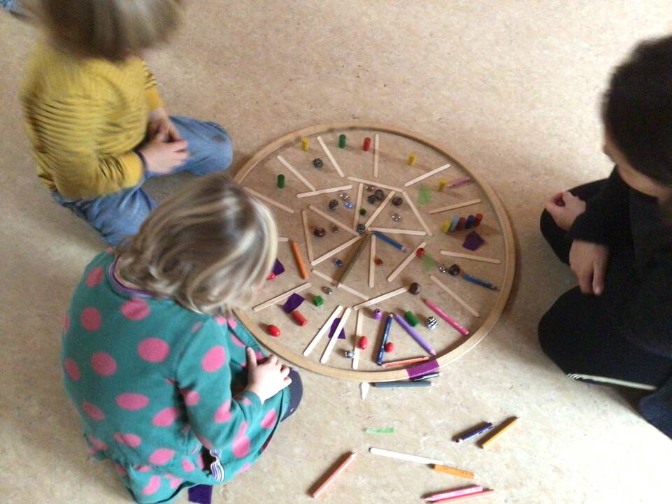 Drei Kinder sitzen um den Holzring mit Stäben.