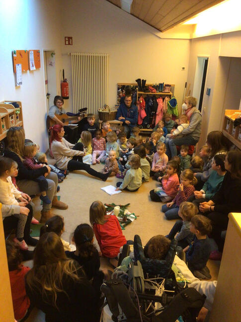 Viele Kinder sitzen um eine Frau mirt einer Gitarre in der Hand.