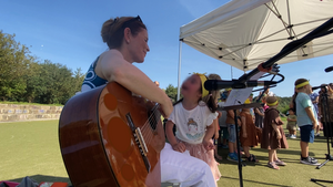 Neben einer Frau mit einer Gitarre ist ein Kind und schaut sie an.