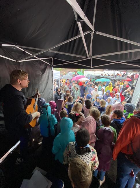 EIn Mann mit einer GItarre unter einem Pavillion davor sehr viele Menschen.