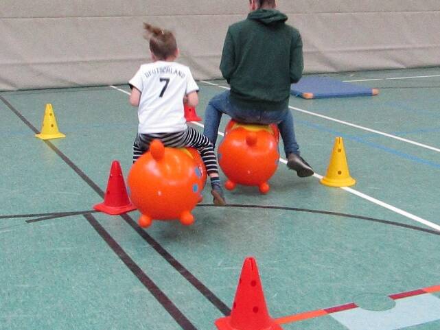 Zwei Personen hüpfen mit Hüpffiguren durch eine Sporthalle.