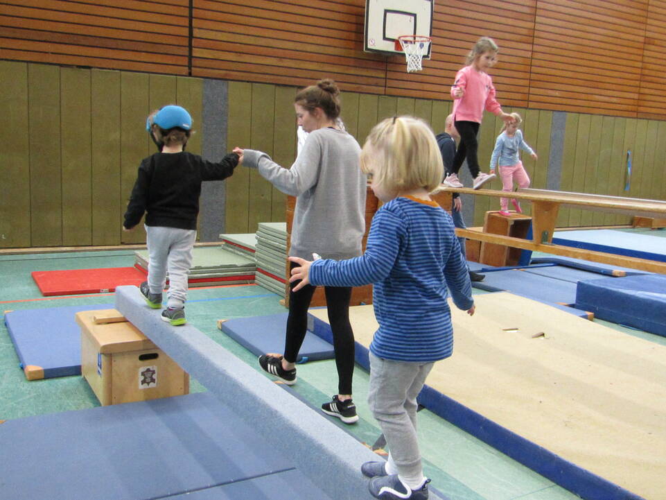 Zwei Kinder balancieren, ein Kind hält dabei die Hand einer jungen Frau.