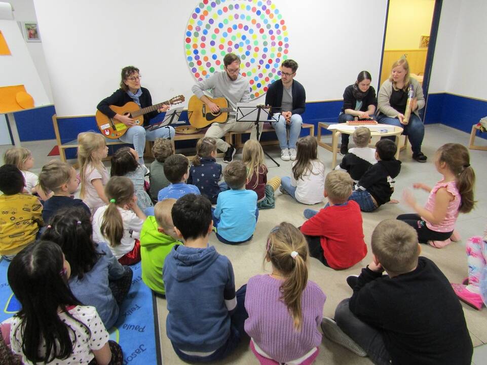 Viele Kinder in einem Raum schauen Musikern zu.