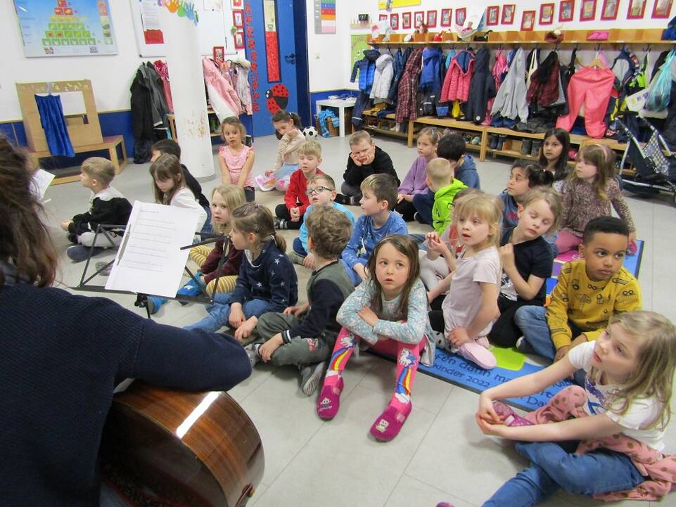 Viele Kinder sitzen auf Matten in einem Raum auf dem Boden.