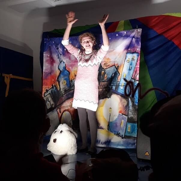 Eine Frau steht vor einem Bild im Lichtschein und hält die Arme hoch.