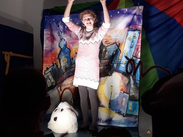 Eine Frau steht vor einem Bild im Lichtschein und hält die Arme hoch.