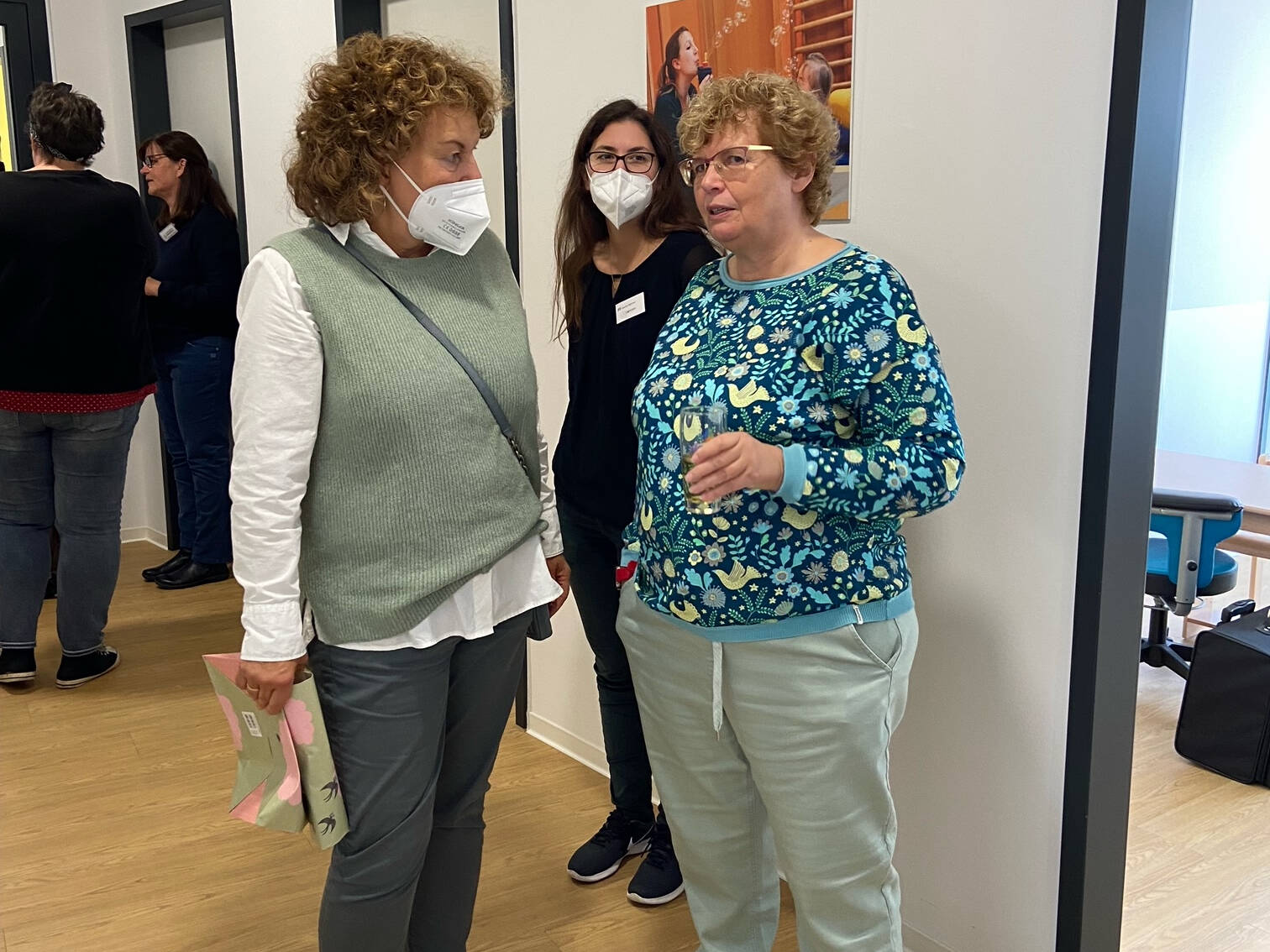 Drei Frauen stehen zusammen, zwei mit Maske.