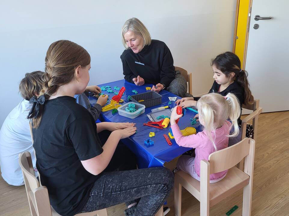 Kinder kneten mit einer erwachsenen Frau und einem älteren Mädchen.