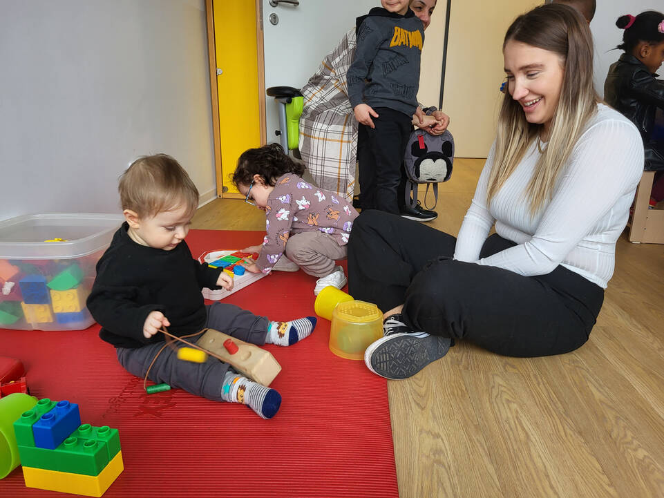 Eine Frau sitzt mit einem Kind auf dem Boden und schaut zu.