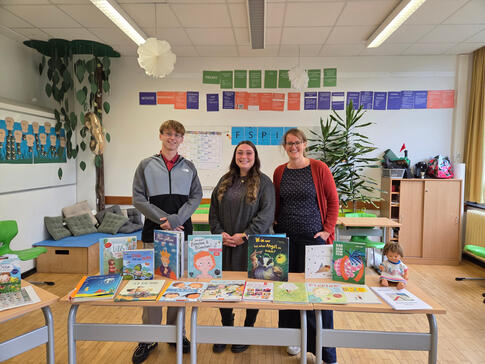 Drei Personen stehen in einem Raum hinter Tischen.