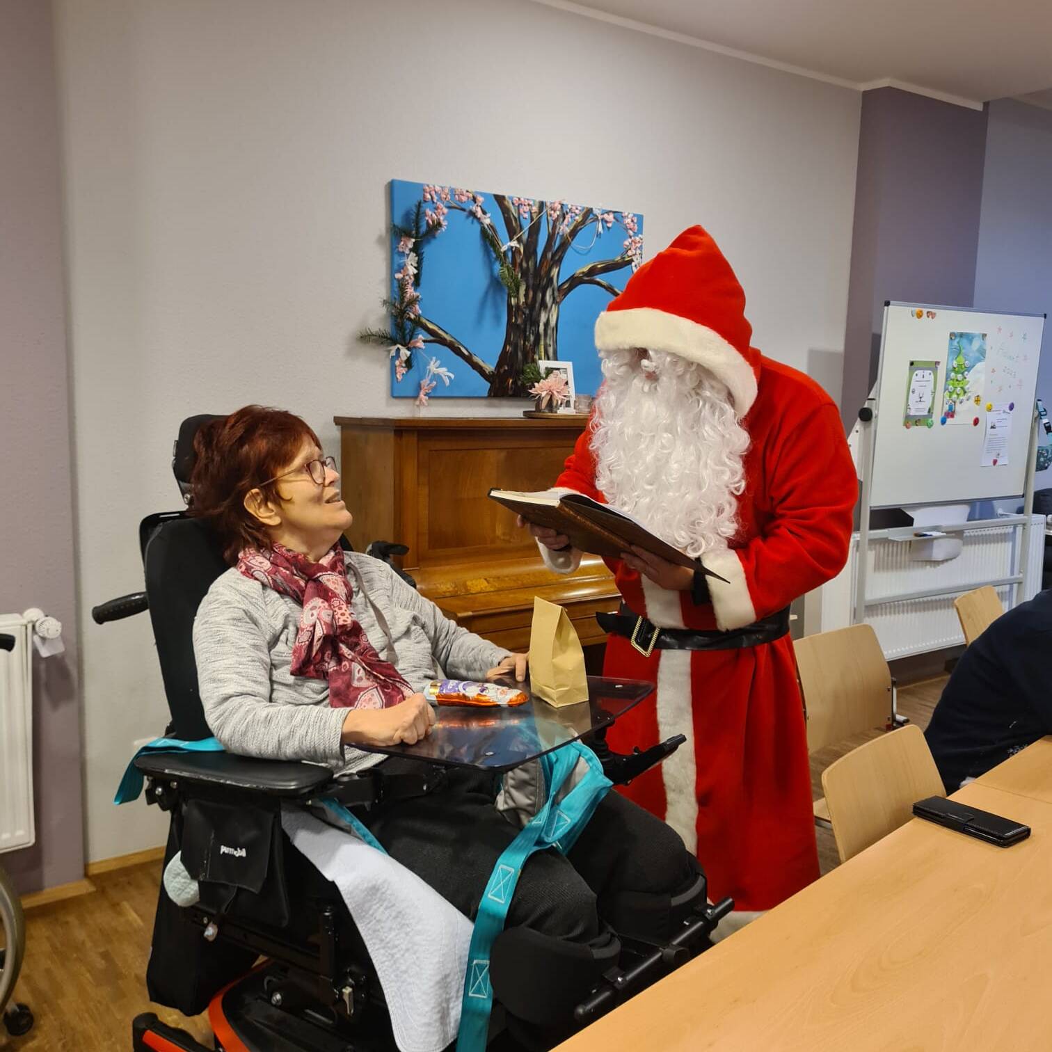 Der Nikolaus sitzt neben einer Frau im Rollstuhl.