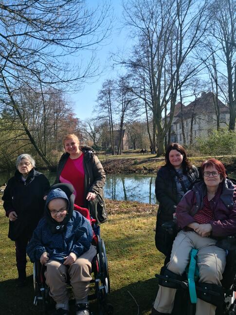 Menschen mit und ohne Hilfesmittel auf einer Wiese vor einem Fluss.