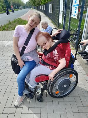 Eine Frau sitzt bei einer Frau im Rollstuhl auf dem Schoß.