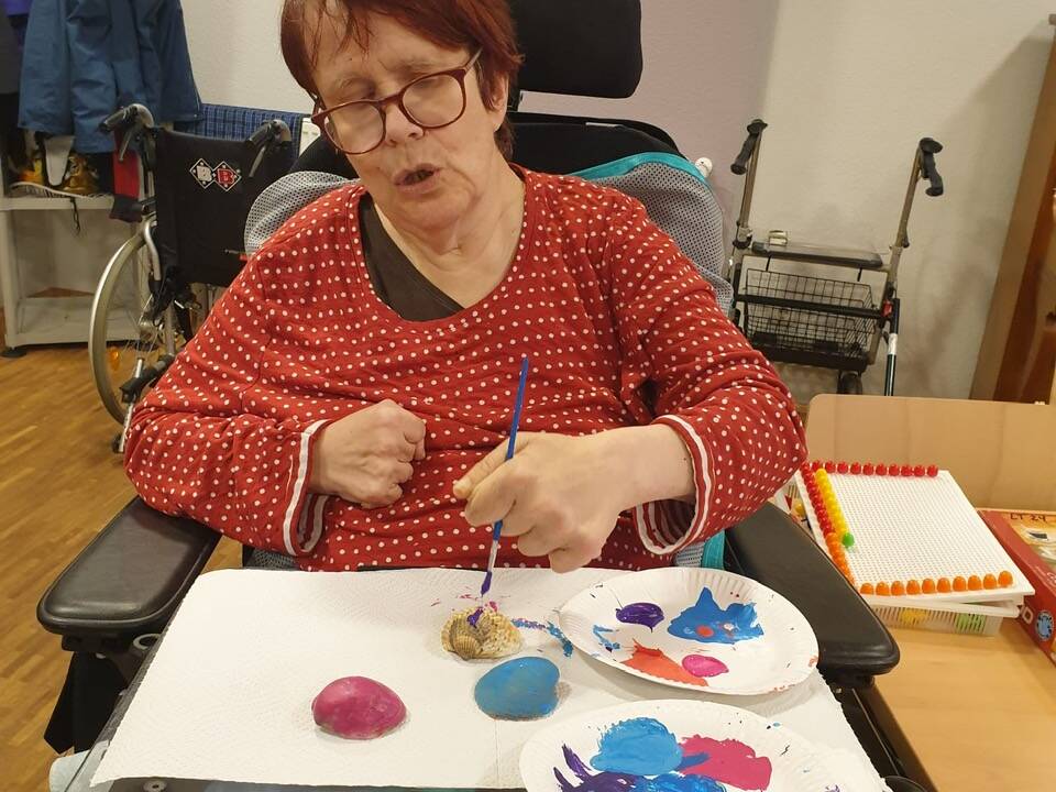 Eine Frau im Rollstuhl arbeitet mit Farbe