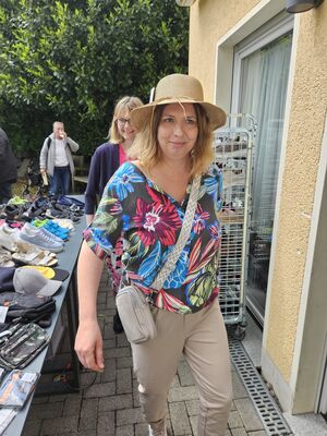 Eine Frau mit Hut und Handtasche vor einem Haus.