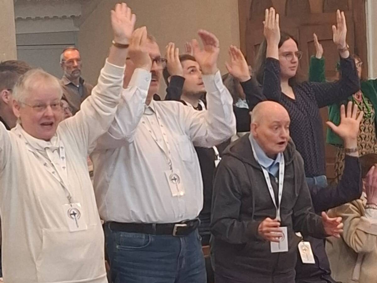 Menschen stehen in der Kirche und strecken die Hände in die Höhe.