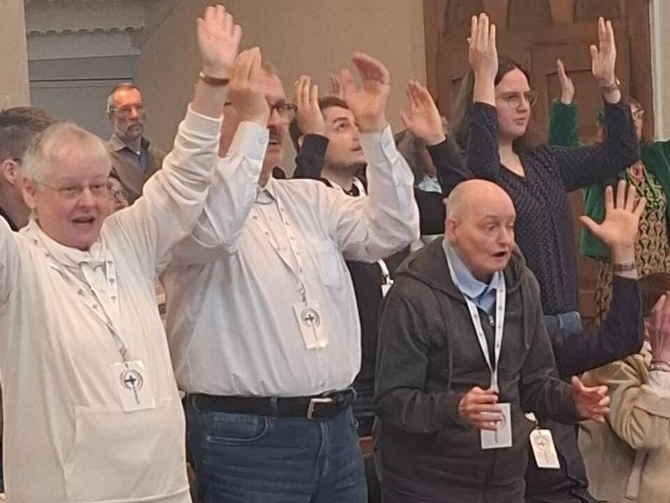 Menschen stehen in der Kirche und strecken die Hände in die Höhe.