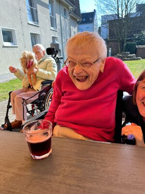 Eine Frau sitzt draussen an einem Tisch, vor ihr steht ein Getränk.
