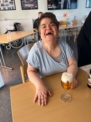 Eine Frau sitzt drinnen an einem Tisch mit einem Bier.