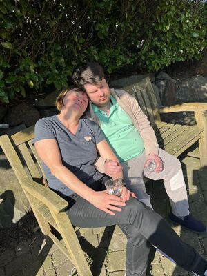 Zwei Personen sonnen sich und sitzen dabei auf einer Holzbank.