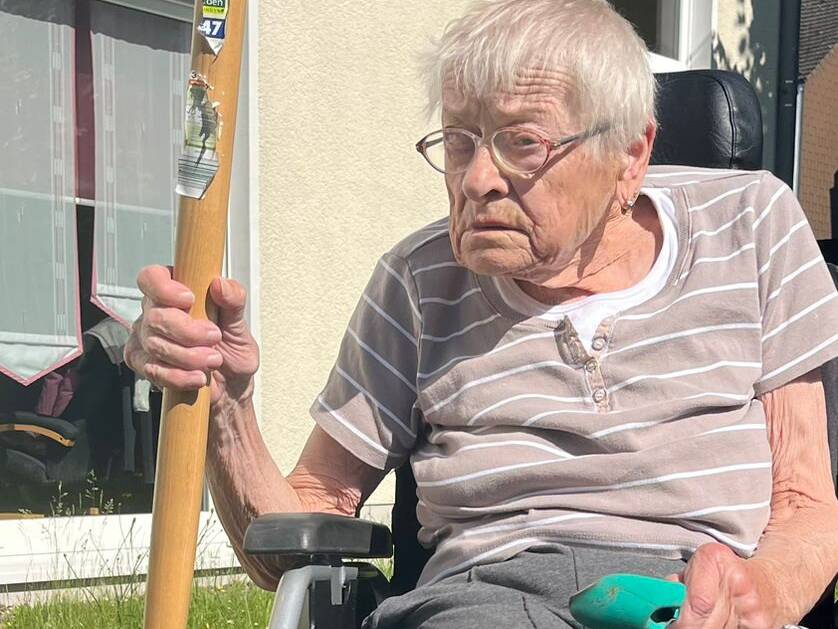 Eine Person im Rollstuhl mit einem Spaten in der Hand.