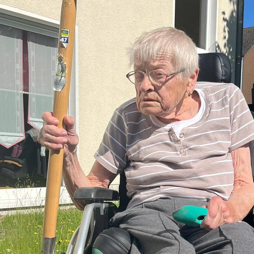 Eine Person im Rollstuhl mit einem Spaten in der Hand.