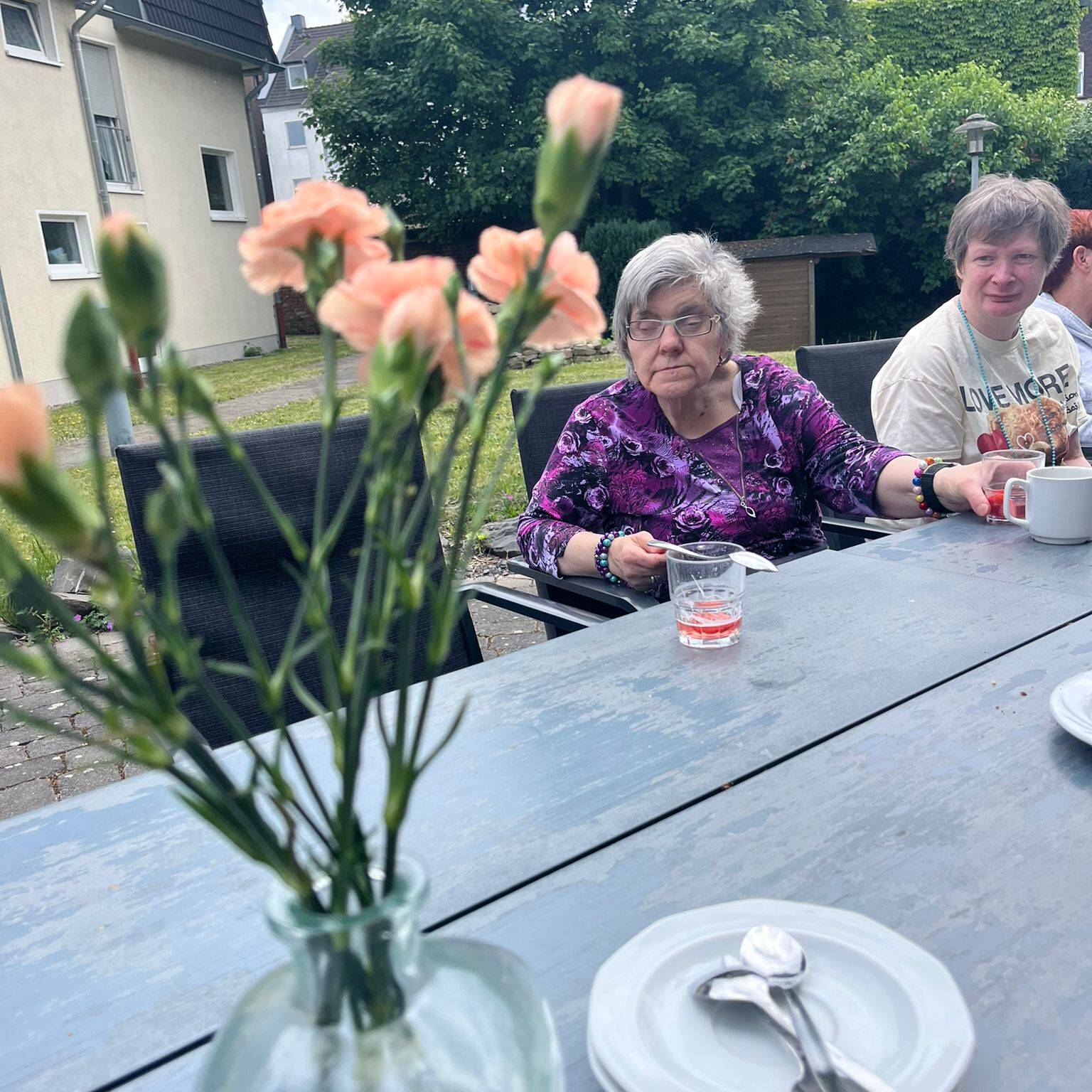 Zwei Frauen sitzen am Tisch, es stehen Blumen auf dem Tisch.