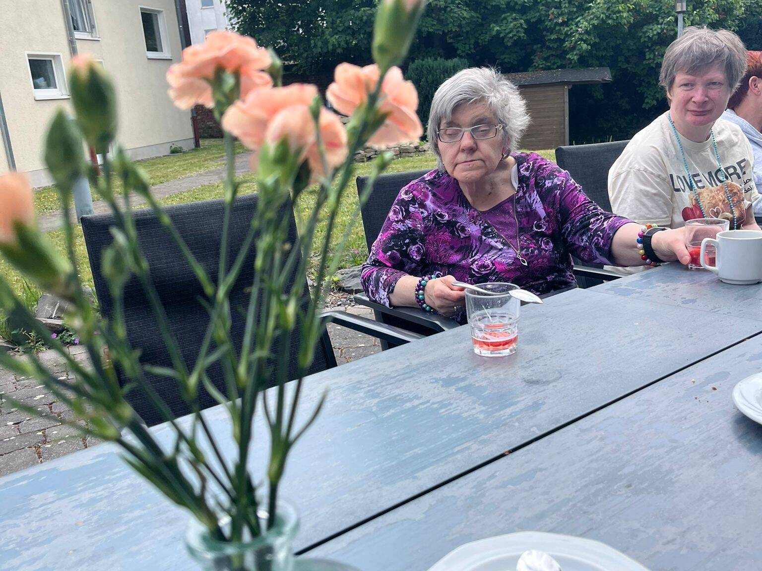 Zwei Frauen sitzen am Tisch, es stehen Blumen auf dem Tisch.
