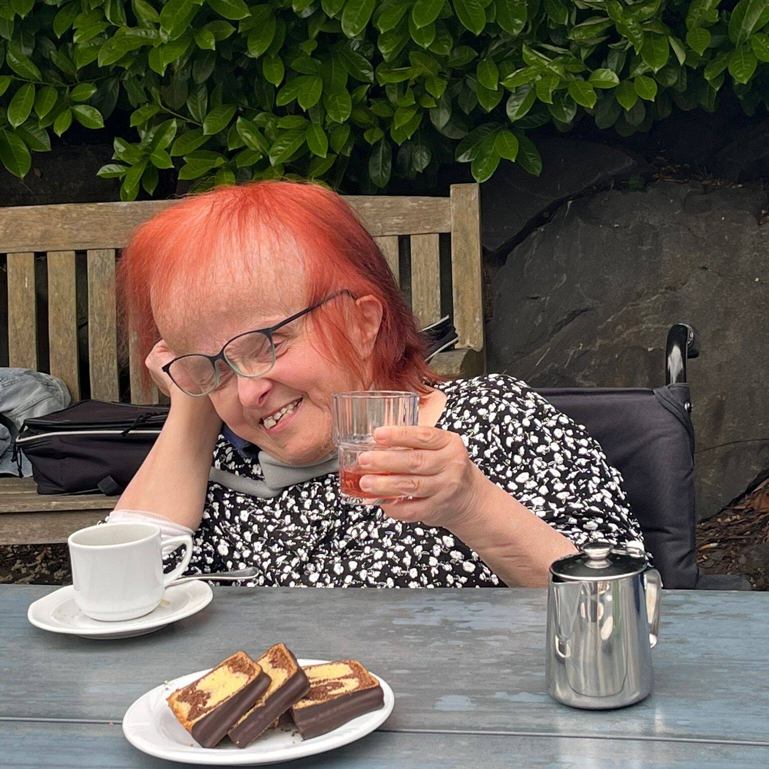 Eine Frau mit roten Haaren sitzt an einem Tisch und hebt ein Glas in die Luft.