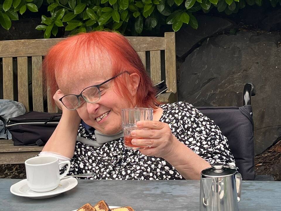 Eine Frau mit roten Haaren sitzt an einem Tisch und hebt ein Glas in die Luft.
