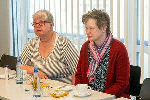 Zwei Frauen sitzen in einem Raum am Tisch.