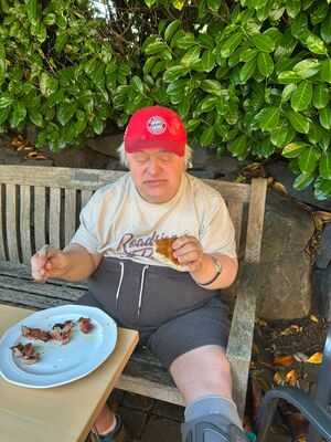 Ein Mann sitzt im Schatten auf einer Bank und isst.