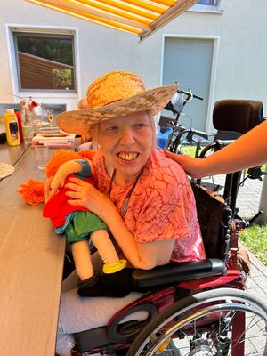 Eine Frau mit Hut und einer Puppe in der Hand im Rollstuhl.