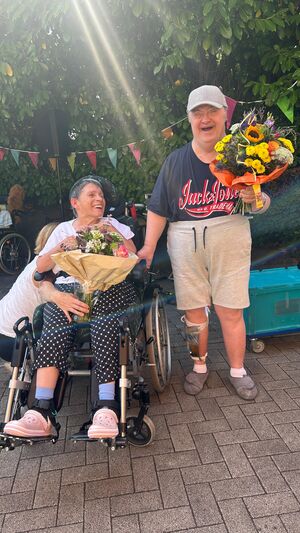 Zwei Personen mit Hilfmittel haben Blumensträuße in der Hand.