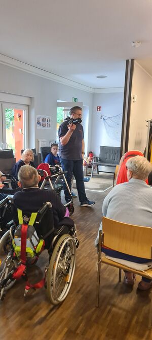 Menschen mit und ohne Hilfsmittel sitzen in einem Raum.