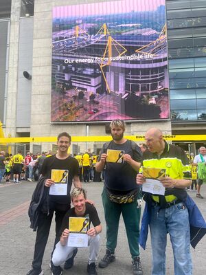 Fans, einer hockt, und ein Begleiter mit Tikets in der Hand, vorm Stadion