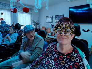 Personen in Rollstühlen, zum Teil mit Masken in einem Raum.