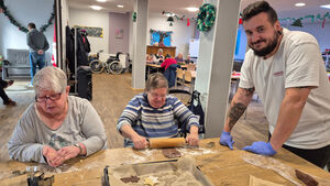 Zwei Frauen machen Plätzchen und ein Mann steht neben dem Tisch.