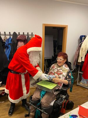 Der Nikolaus übergibt einer Frau im Rollstuhl ein Geschenk.