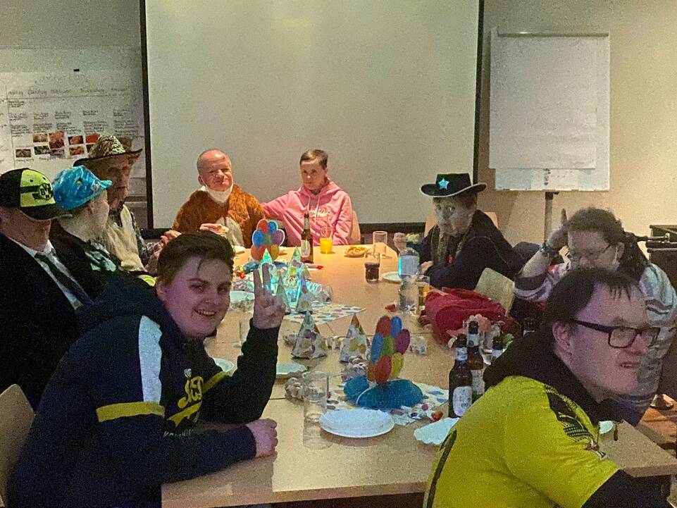 Mehrere Personen sitzen, verkleidet an einem langen Tisch.
