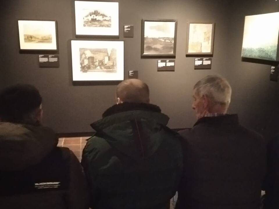 Drei Personen vor einer Wand mit Bildern.