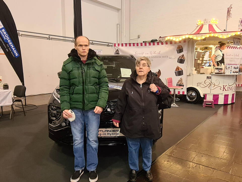 Zwei Personen stehen in einer Halle vor einem dunklen Auto.