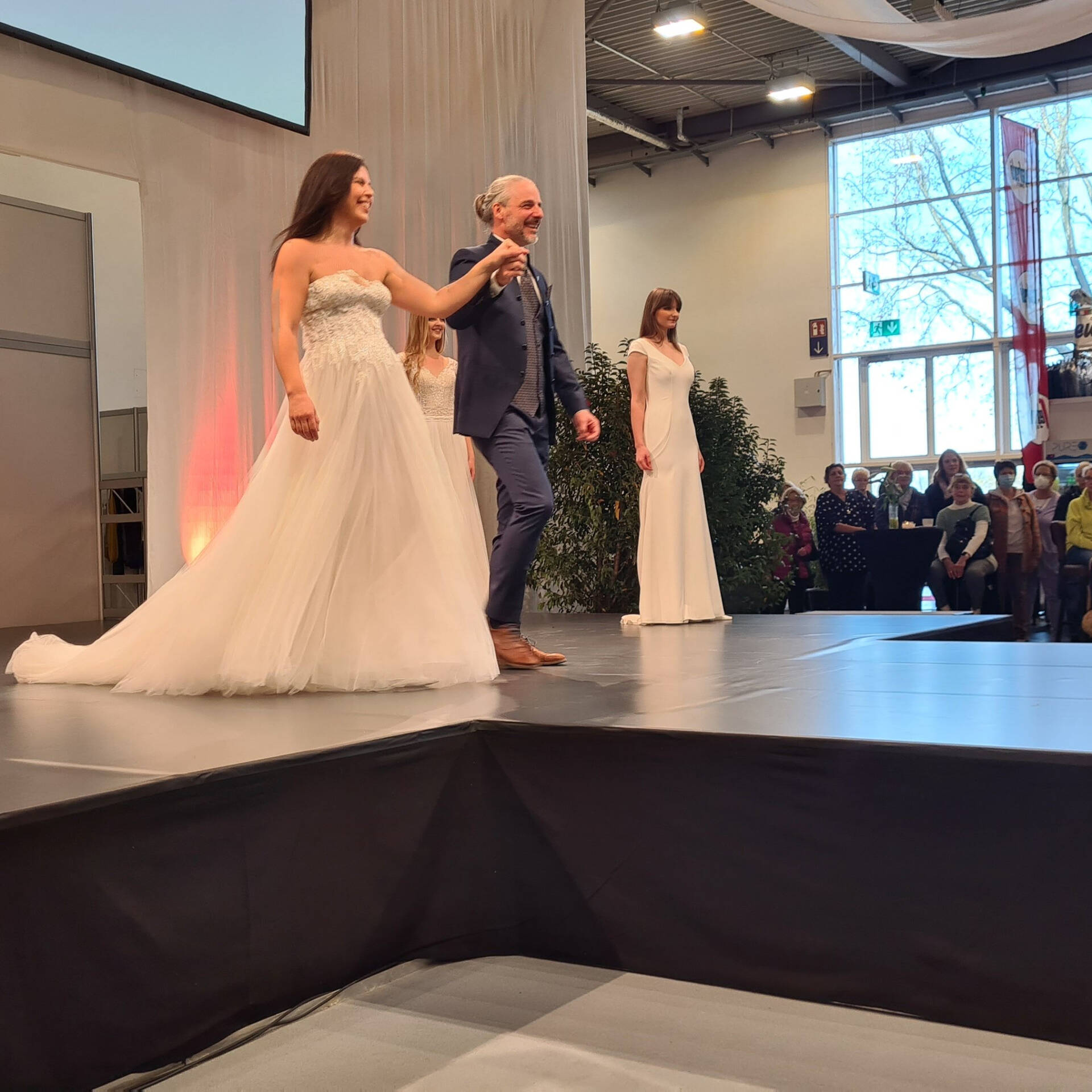 Models mit Brautkleidern, eine Model wird von einem Mann geführt.