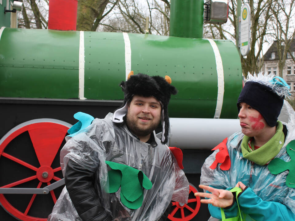 Zwei kostümierte Personen vor einem Karnevalswagen