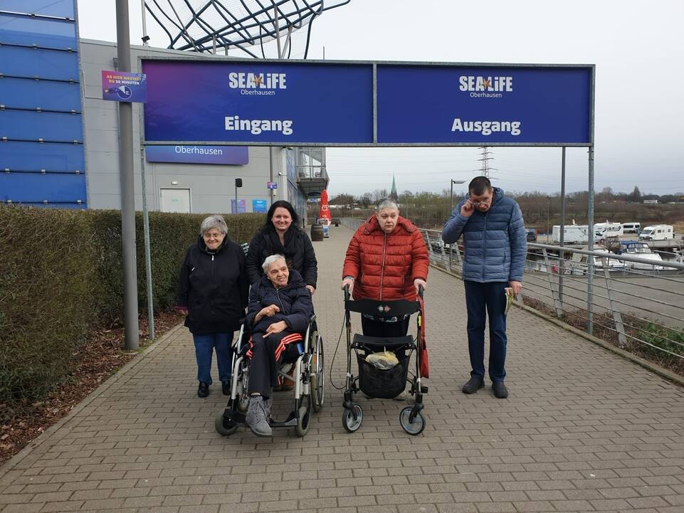 Eine Gruppe Menschen mit Hilfsmittel vor dem Eingang.